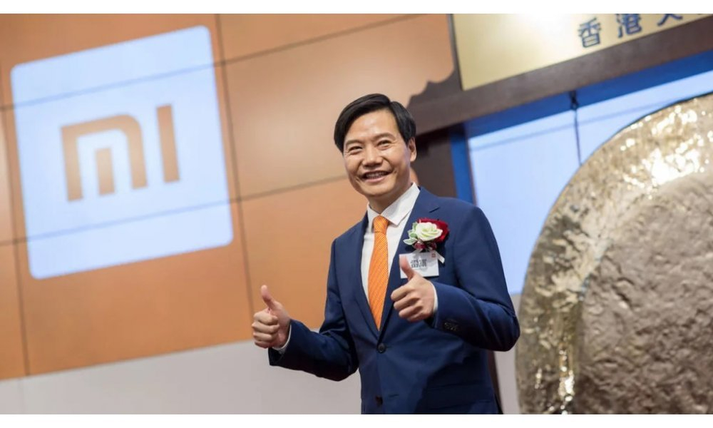 ليو جون مؤسسة شركة شاومي يرفع يديه برمز النجاح وخلفة خائط مرسوم عليه شعار شركة شاومي