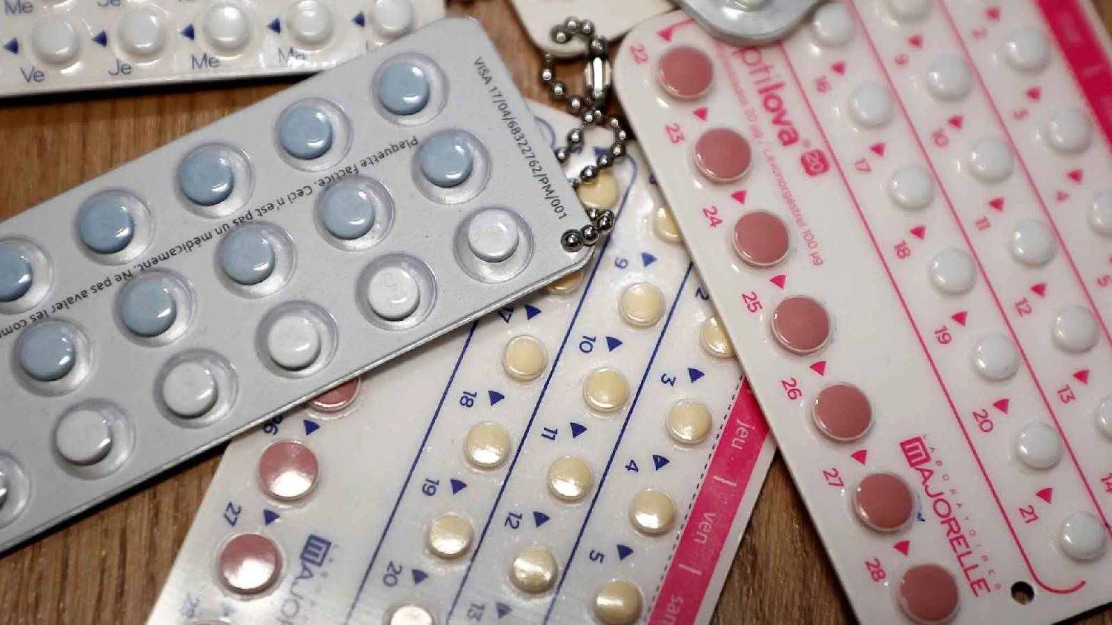 على طاولة بنية يظهر مجموعة من شرائط حبوب منع الحمل بألوان زهري واصفر و ابيض 